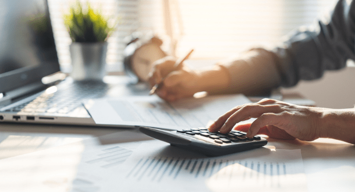 Person using a calculator and reviewing financial documents at a desk with a laptop